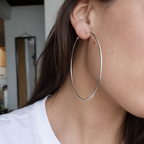 Person wearing a silver hoop earring with a neutral background