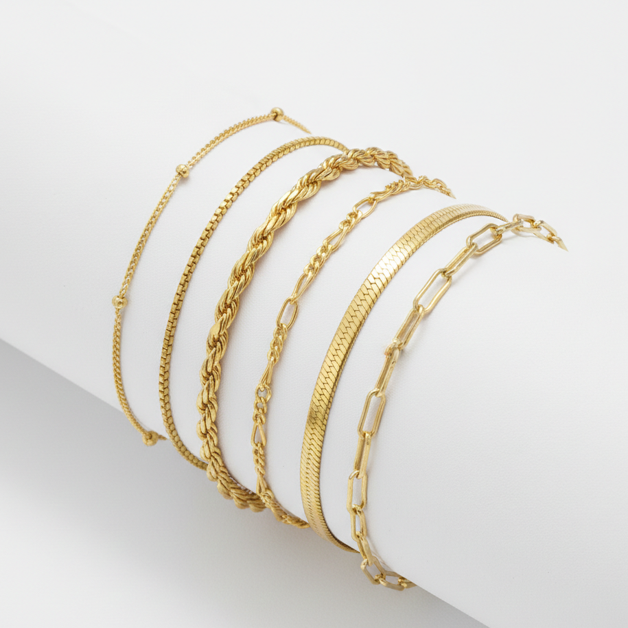 Set of gold bracelets on a white cylindrical object with a light gray background