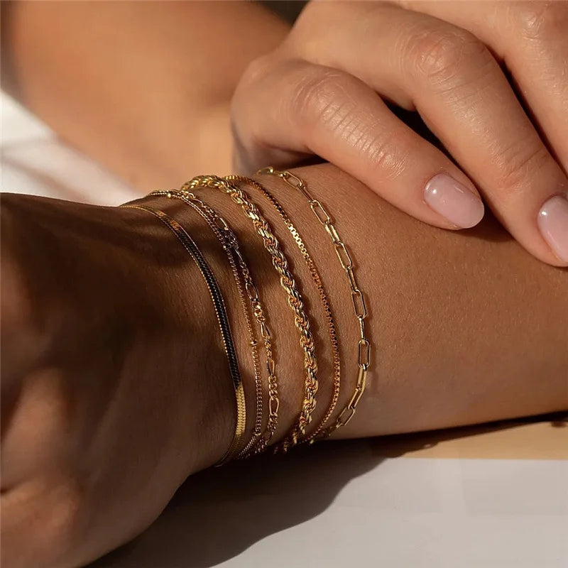 Close-up of a wrist wearing multiple gold bracelets on a neutral background