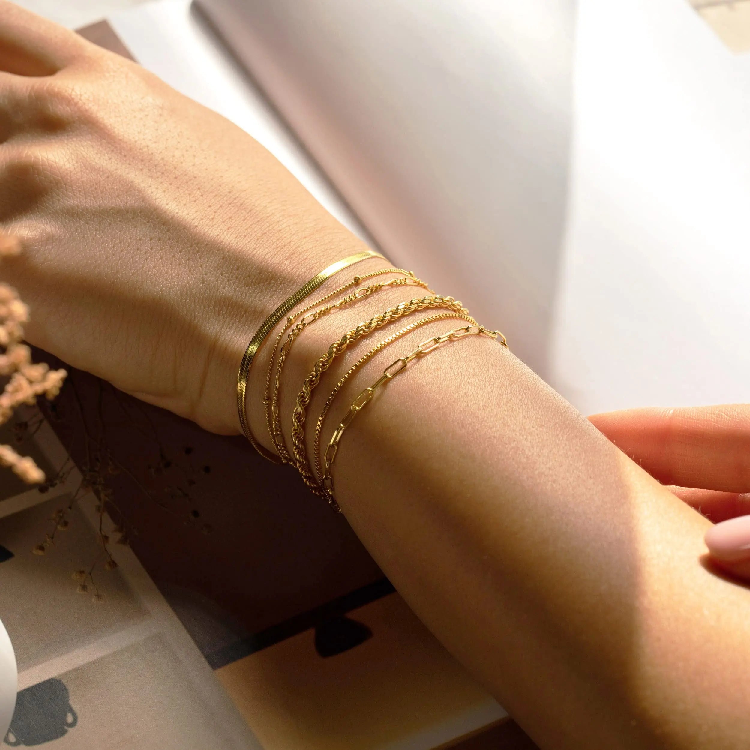 Close-up of a wrist wearing multiple gold bracelets with a blurred background.