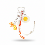 Novelty fried egg and croissant food charm on a keychain with white and orange-red cord detail.