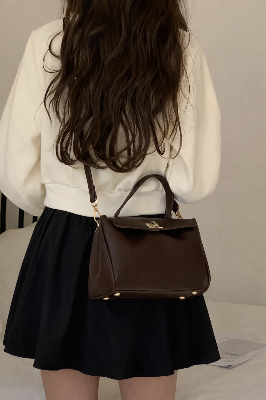 Person wearing a white sweater and black skirt with a brown handbag.