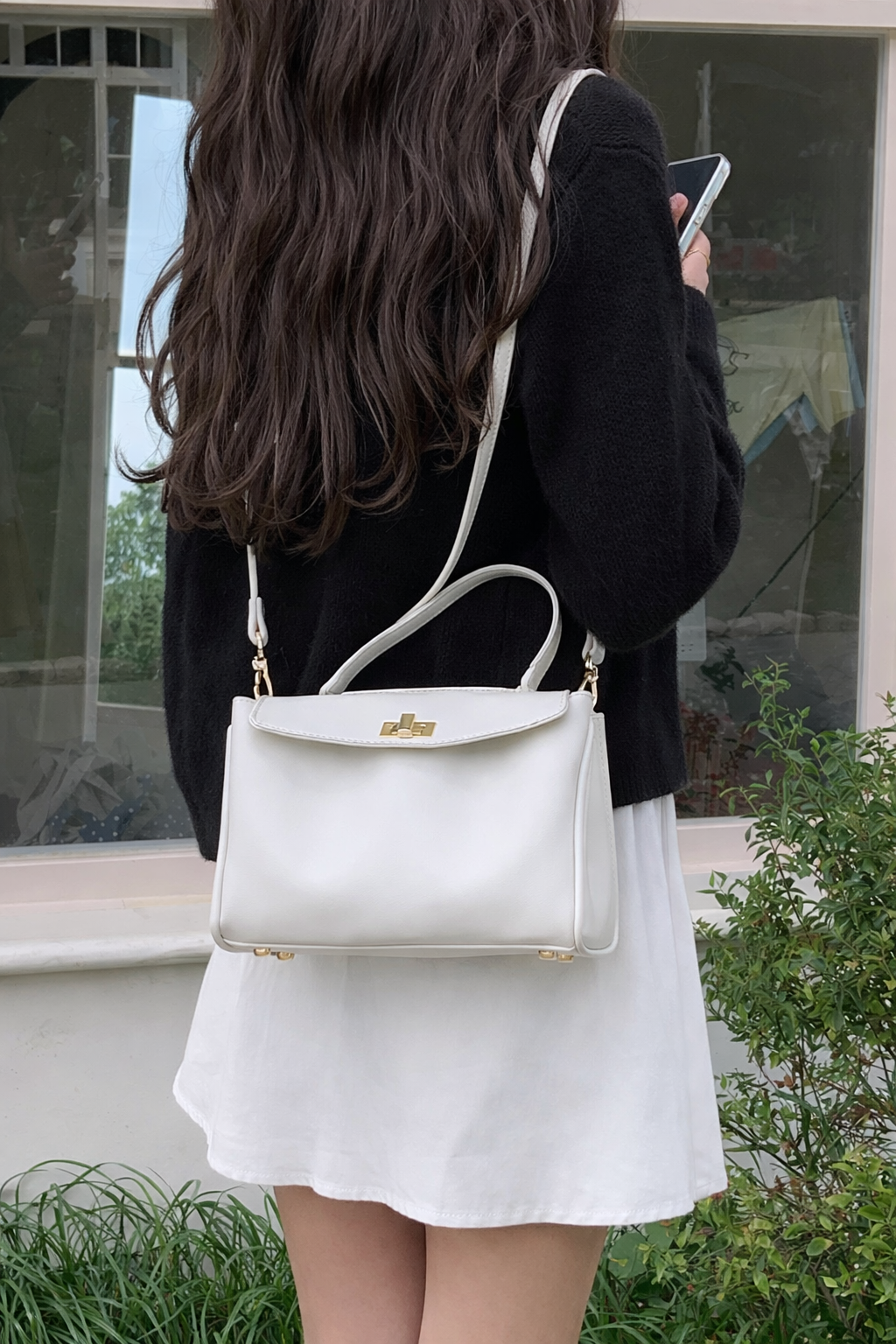 Person wearing a white handbag with gold accents outdoors