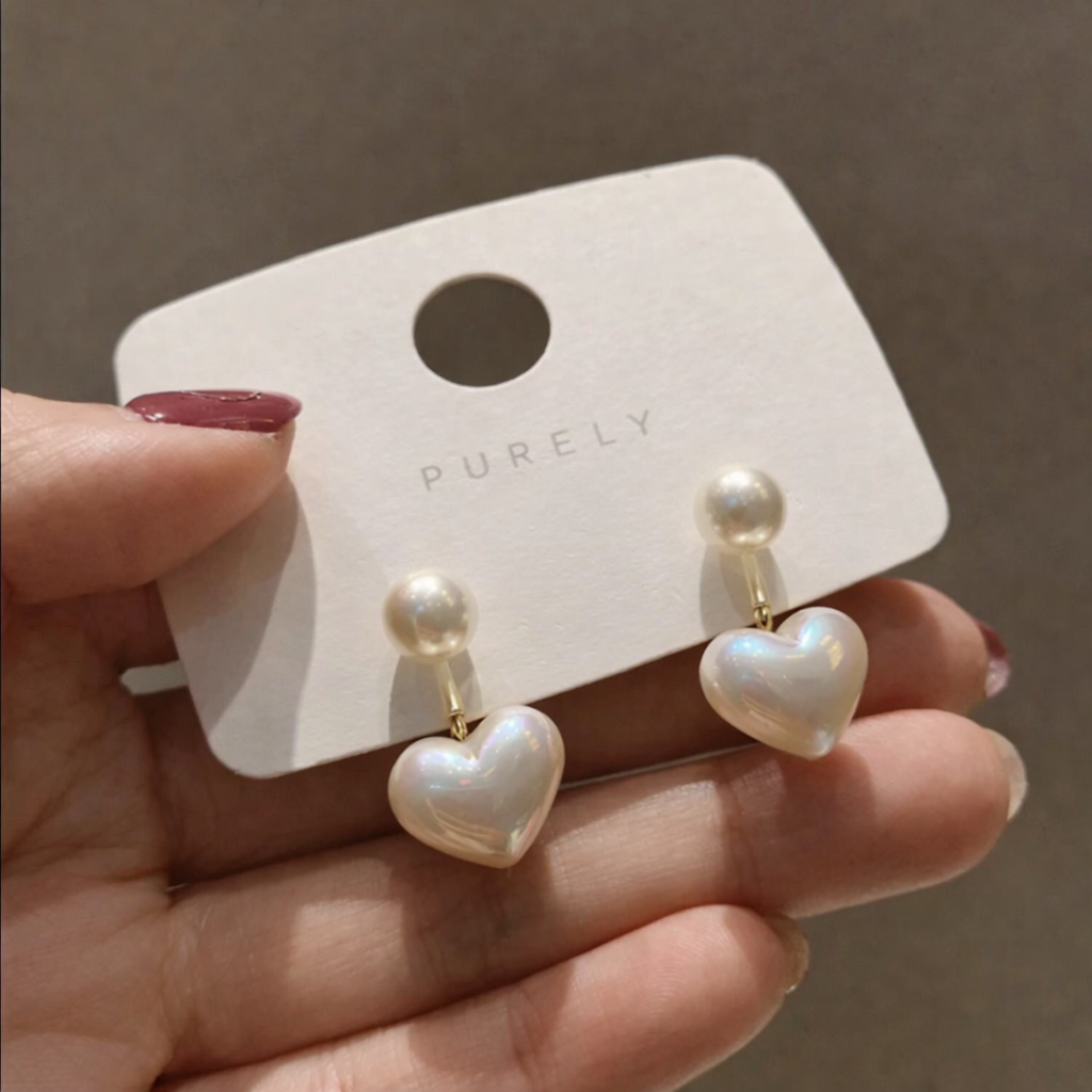 Heart-shaped pearl earrings on a 'PURELY' branded card held by a hand.
