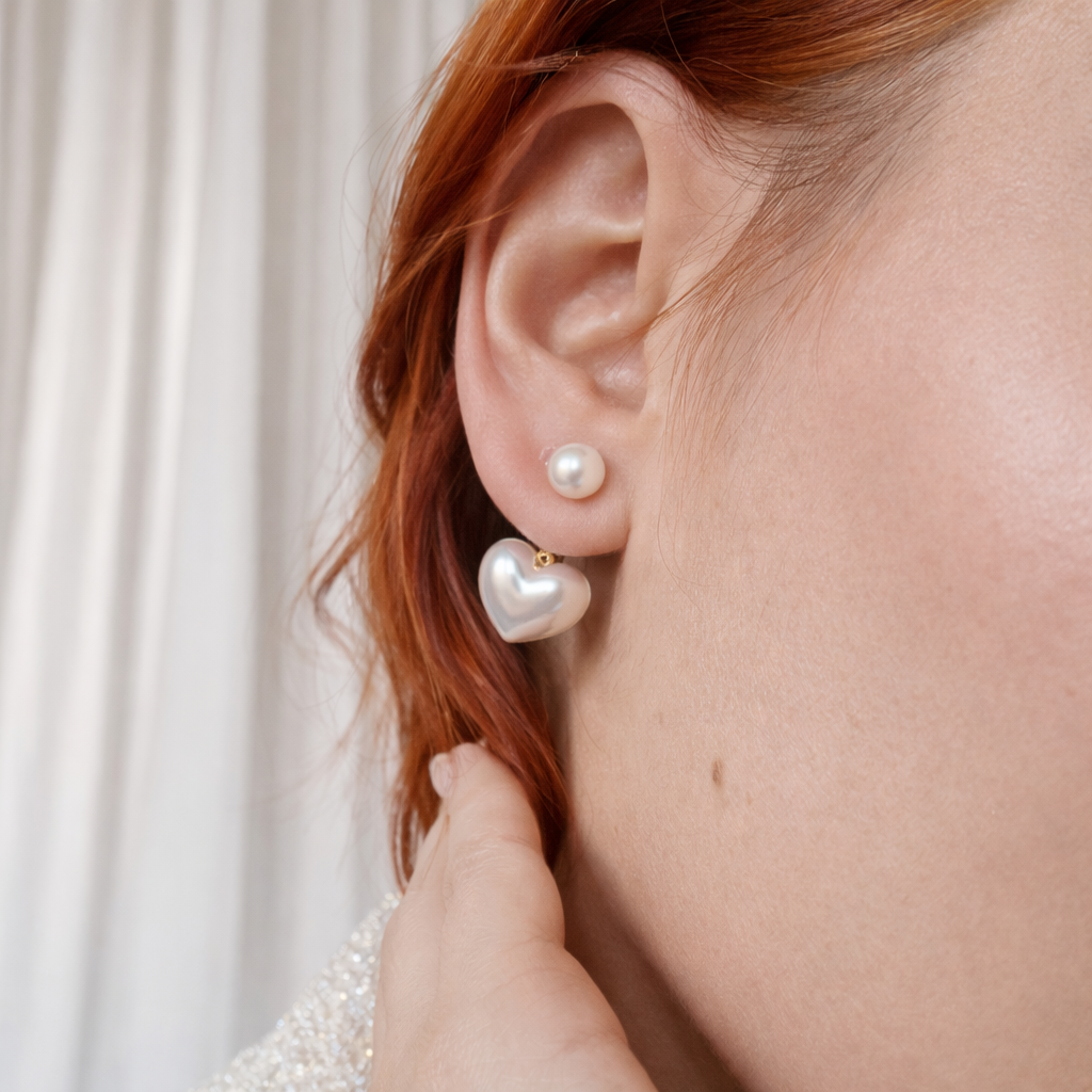 Pearl heart-shaped earrings being worn by a person with red hair.