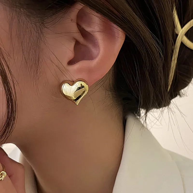 Gold heart-shaped earring worn by a person with brown hair.