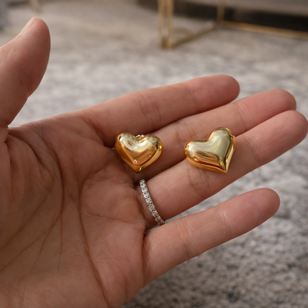 Gold heart-shaped earrings held in a hand with a blurred background