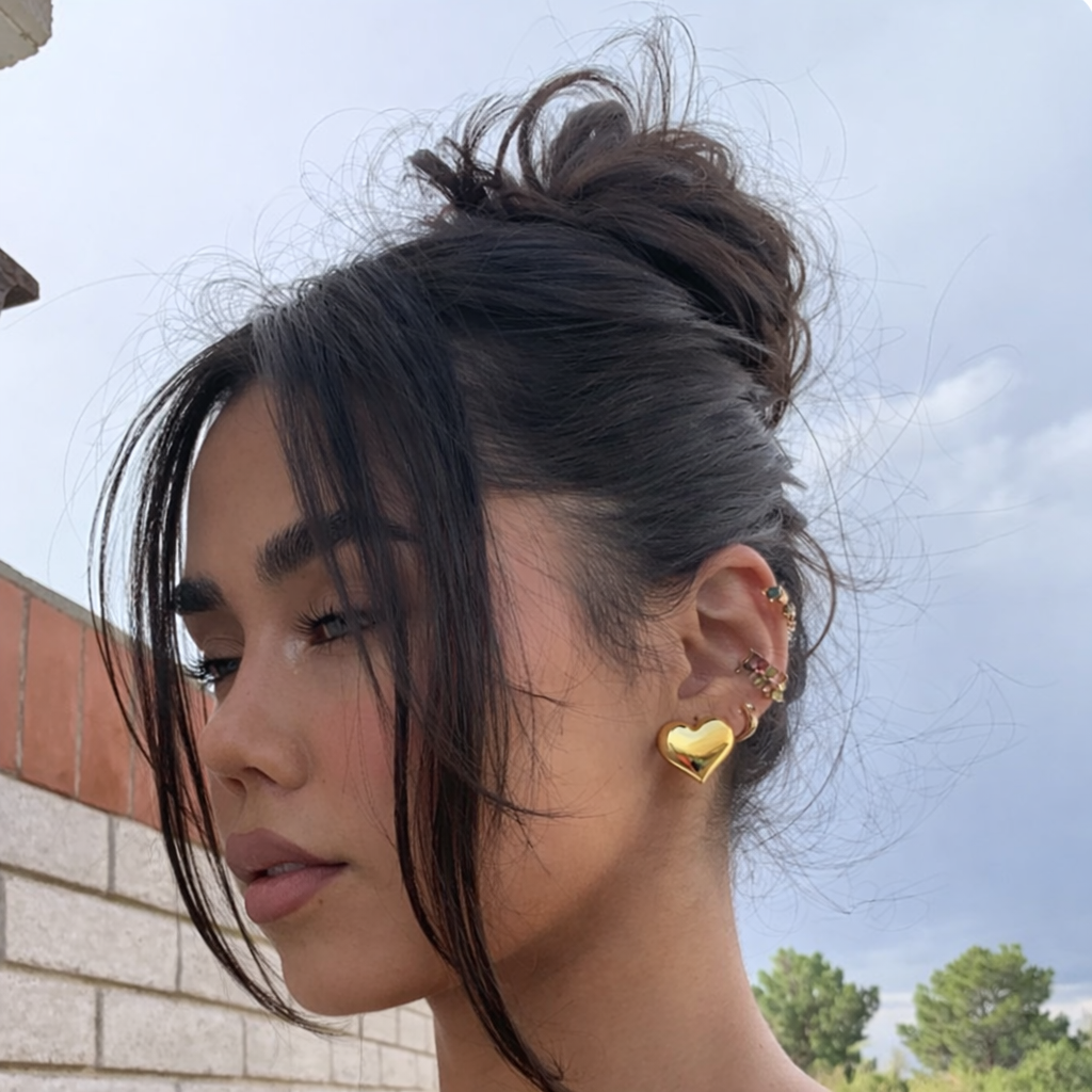 Woman wearing gold heart-shaped earrings with a blurred background