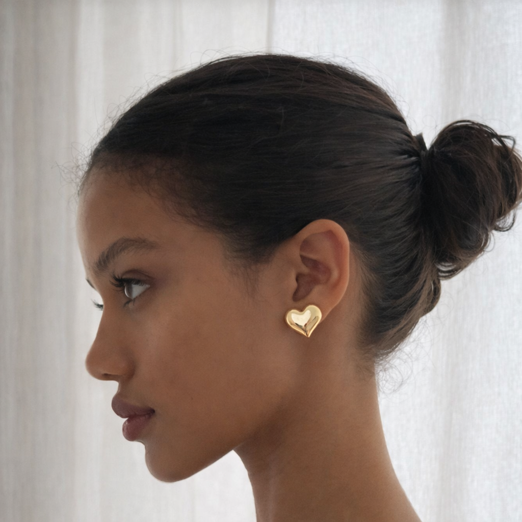 Woman wearing gold heart-shaped earrings with a white curtain background
