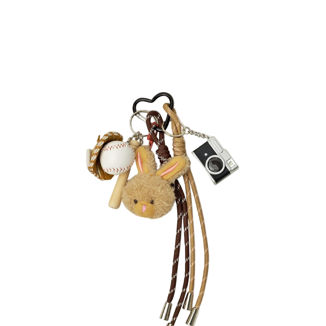 Tan plush bunny bag charm with miniature baseball, baseball bat, glove, and vintage camera components hanging from a keychain.