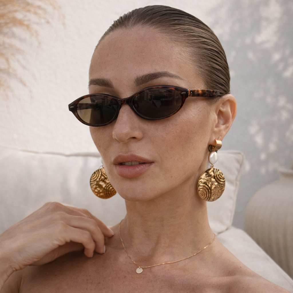 Woman wearing sunglasses and gold earrings with a neutral background