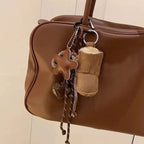 Brown leather handbag with decorative keychain on a neutral background
