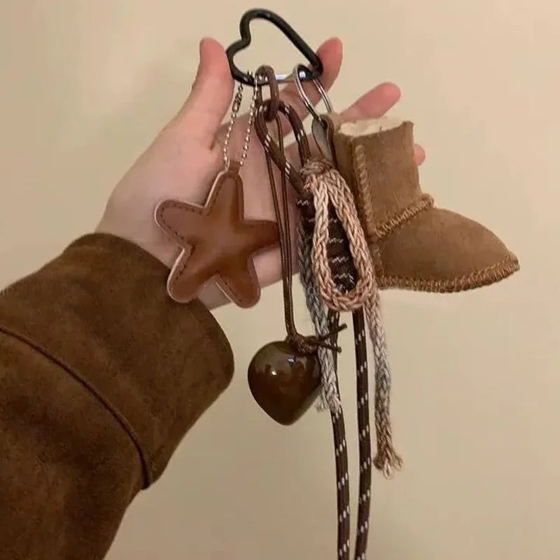 Hand holding a keychain with various brown charms against a beige background