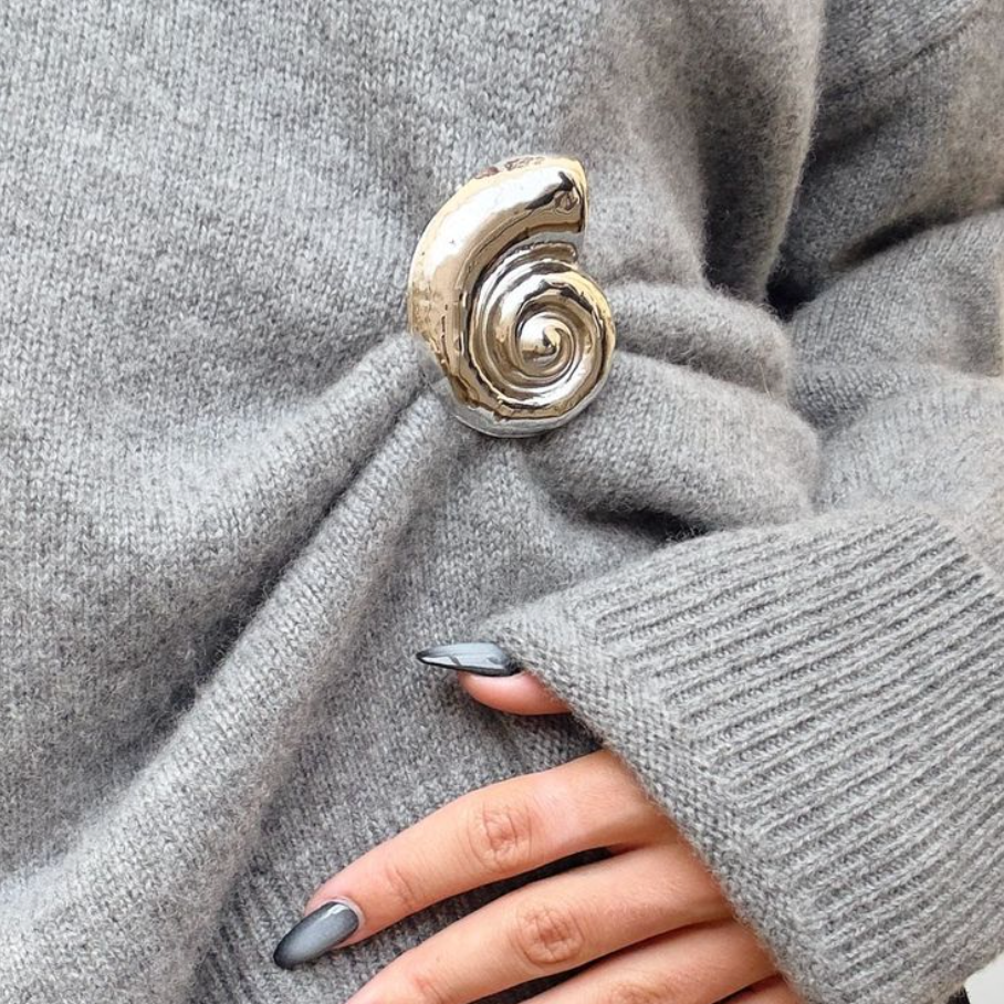 Silver spiral brooch on a gray sweater with a hand wearing a gray sleeve.