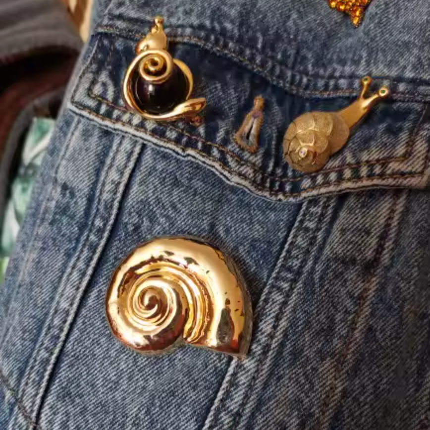 Close-up of a denim jacket with gold shell-shaped pins.