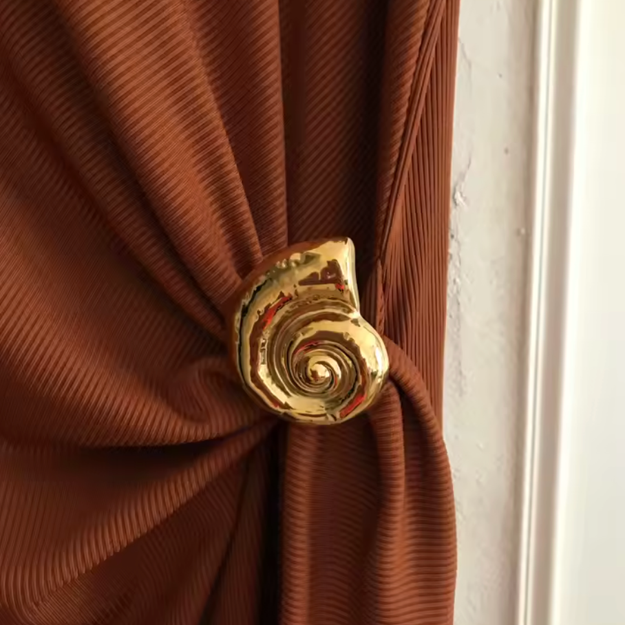 Brown pleated curtain with a gold decorative tie-back against a white wall.
