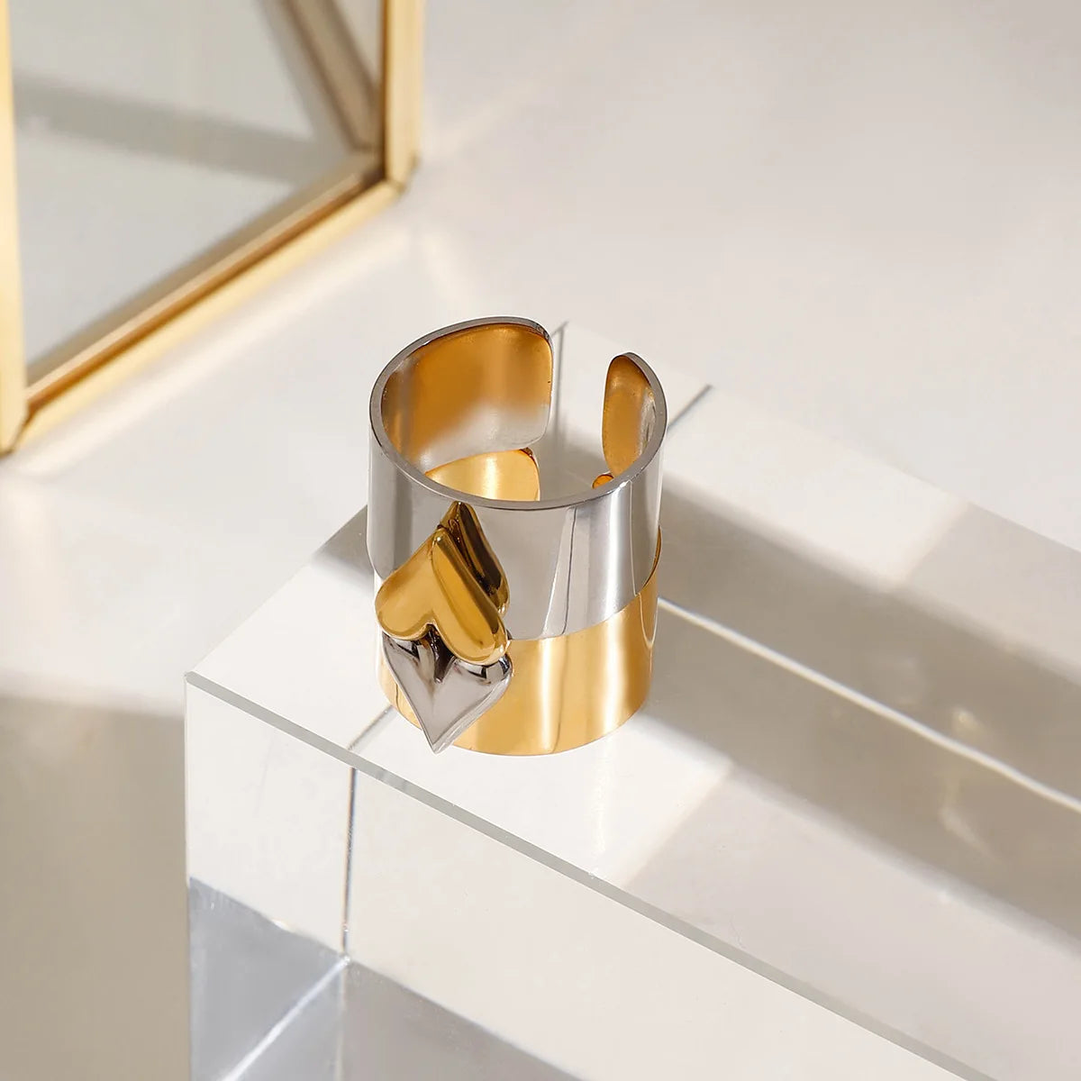 Gold and silver cuff bracelet on a reflective surface with a geometric mirror in the background