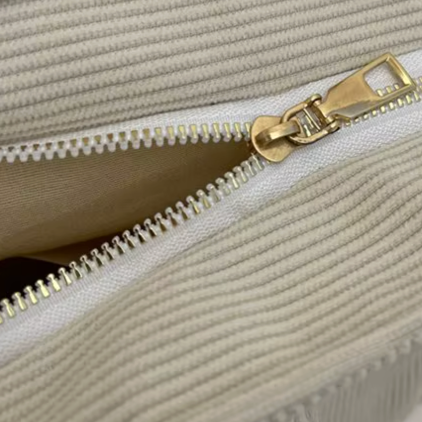 Close-up of a beige textured bag with a gold zipper.