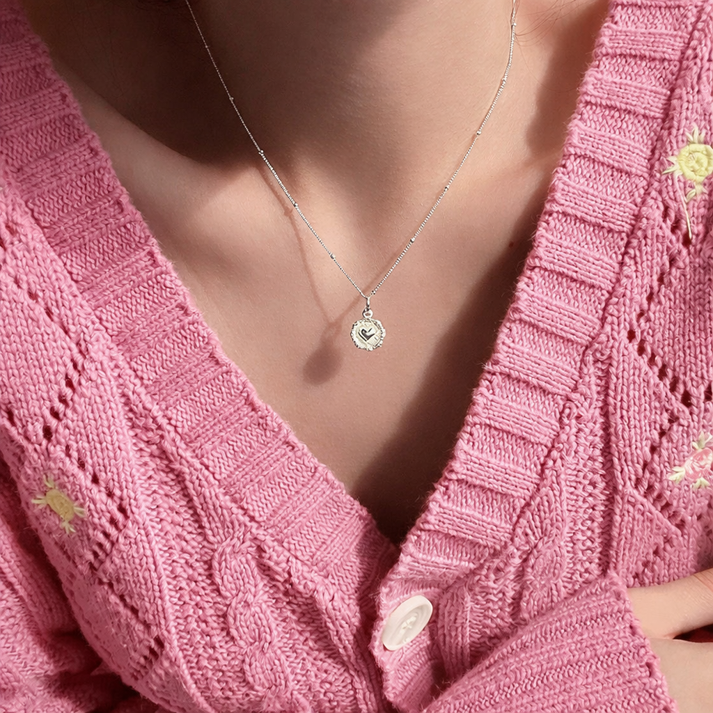 Necklace with a heart pendant worn by a person in a pink knitted cardigan.