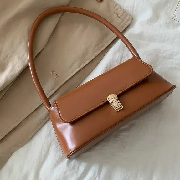 Brown vegan leather handbag with a gold clasp on a light background