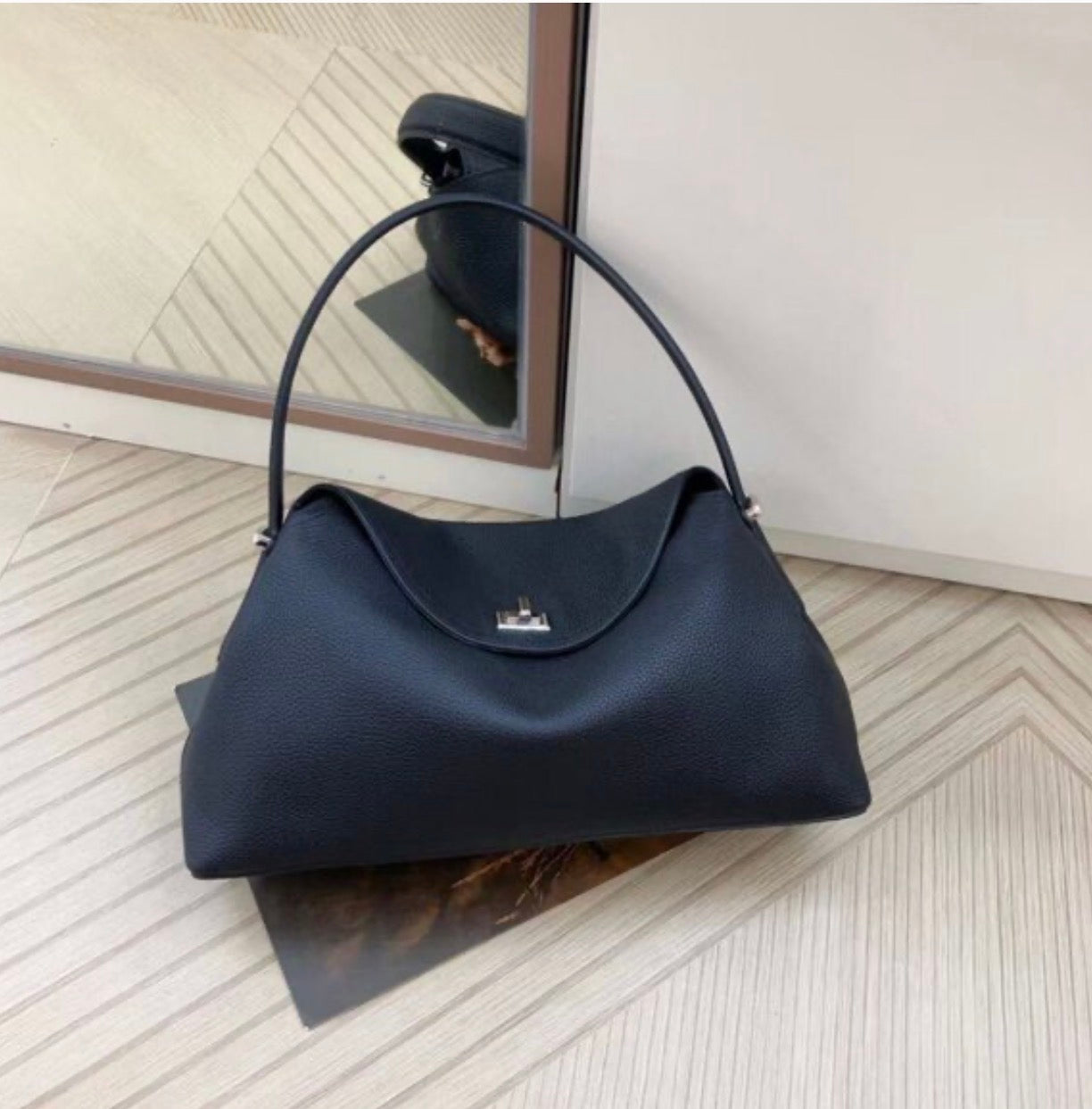 Black handbag on a wooden floor with a mirror reflection