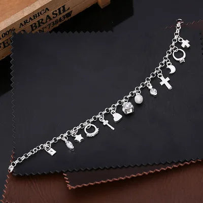 Silver anklet with various charms on a dark surface