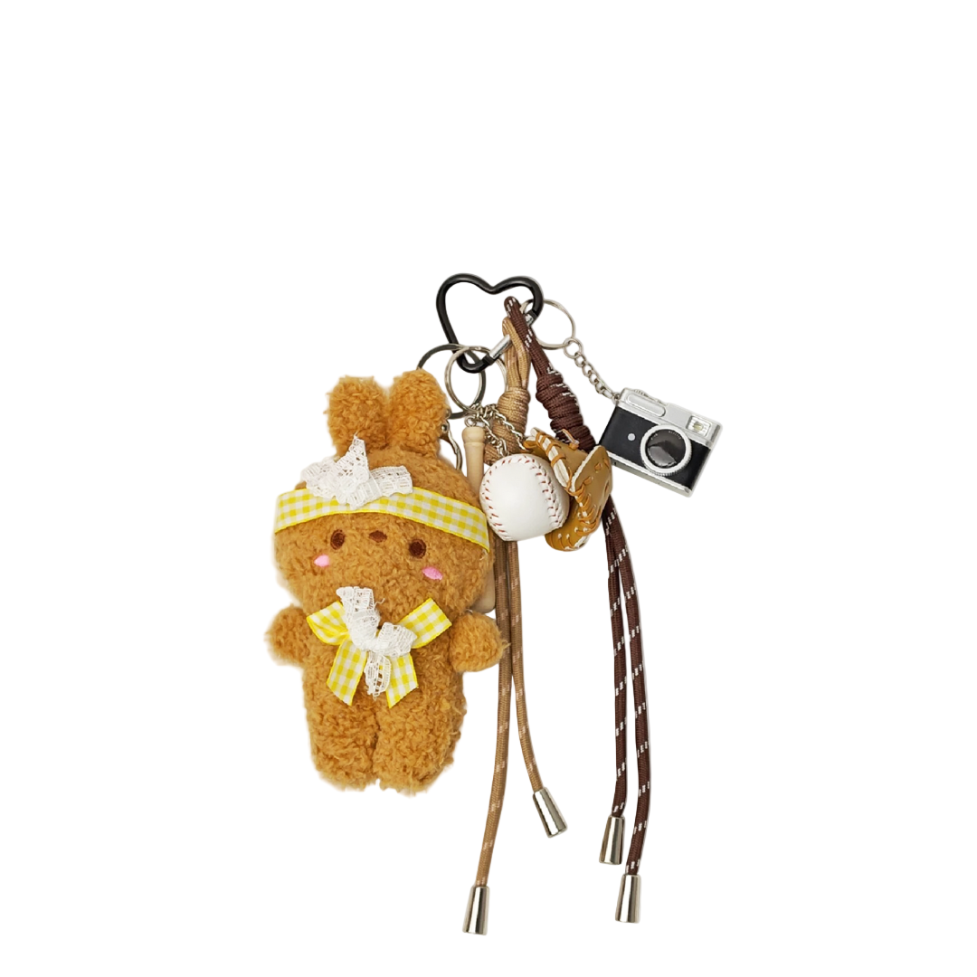 Brown plush bunny bag charm wearing a yellow patterned ribbon, paired with a baseball, baseball glove, and silver camera components hanging from a keychain.