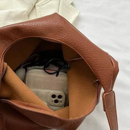 Brown leather handbag with a phone inside, on a white surface with 'THEDETAILSSHOW' branding.