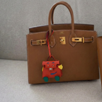 Brown leather handbag with a colorful charm on a neutral background