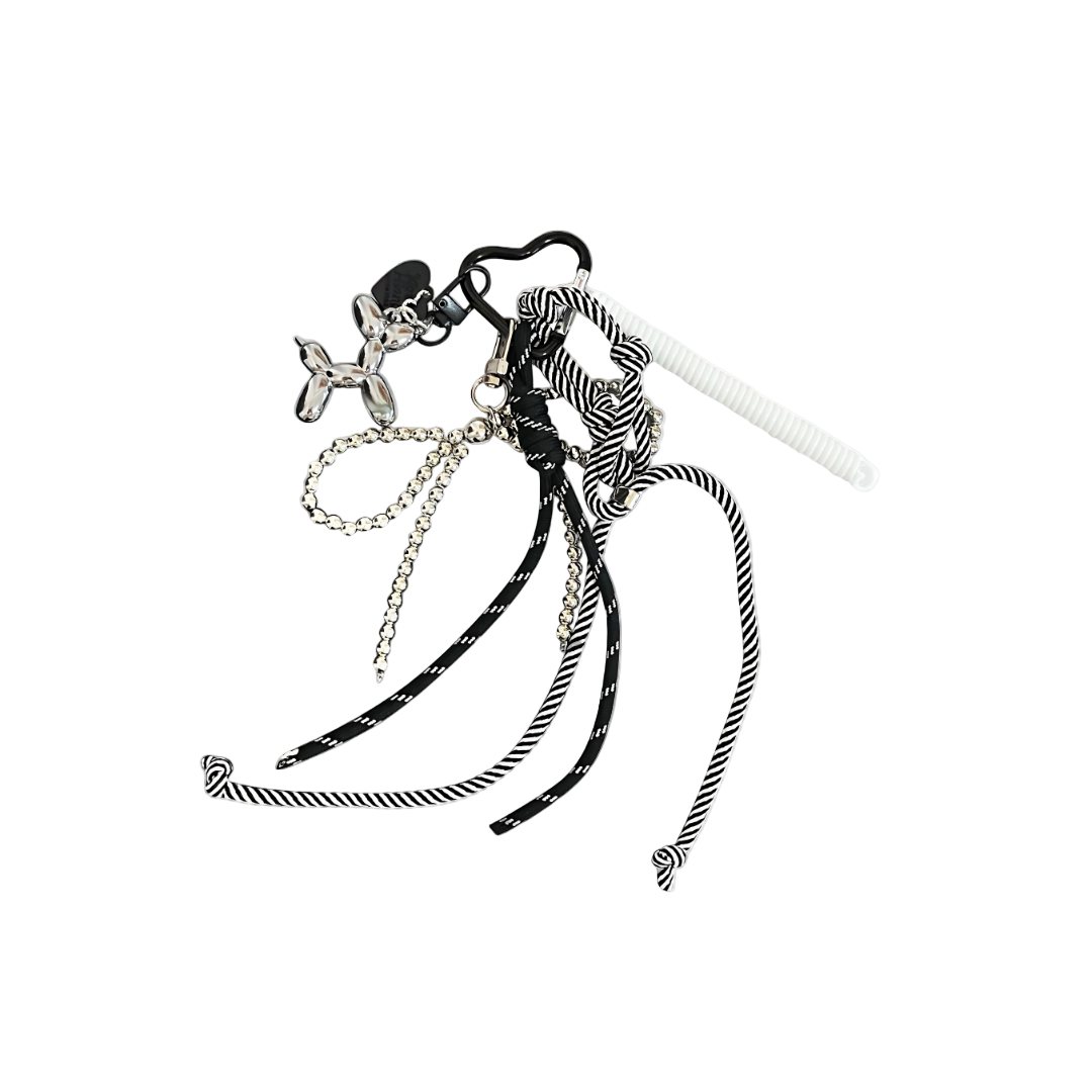 Chrome metallic balloon dog sculpture bag charm linked to a chain and black and white knotted cords hanging from a keychain.
