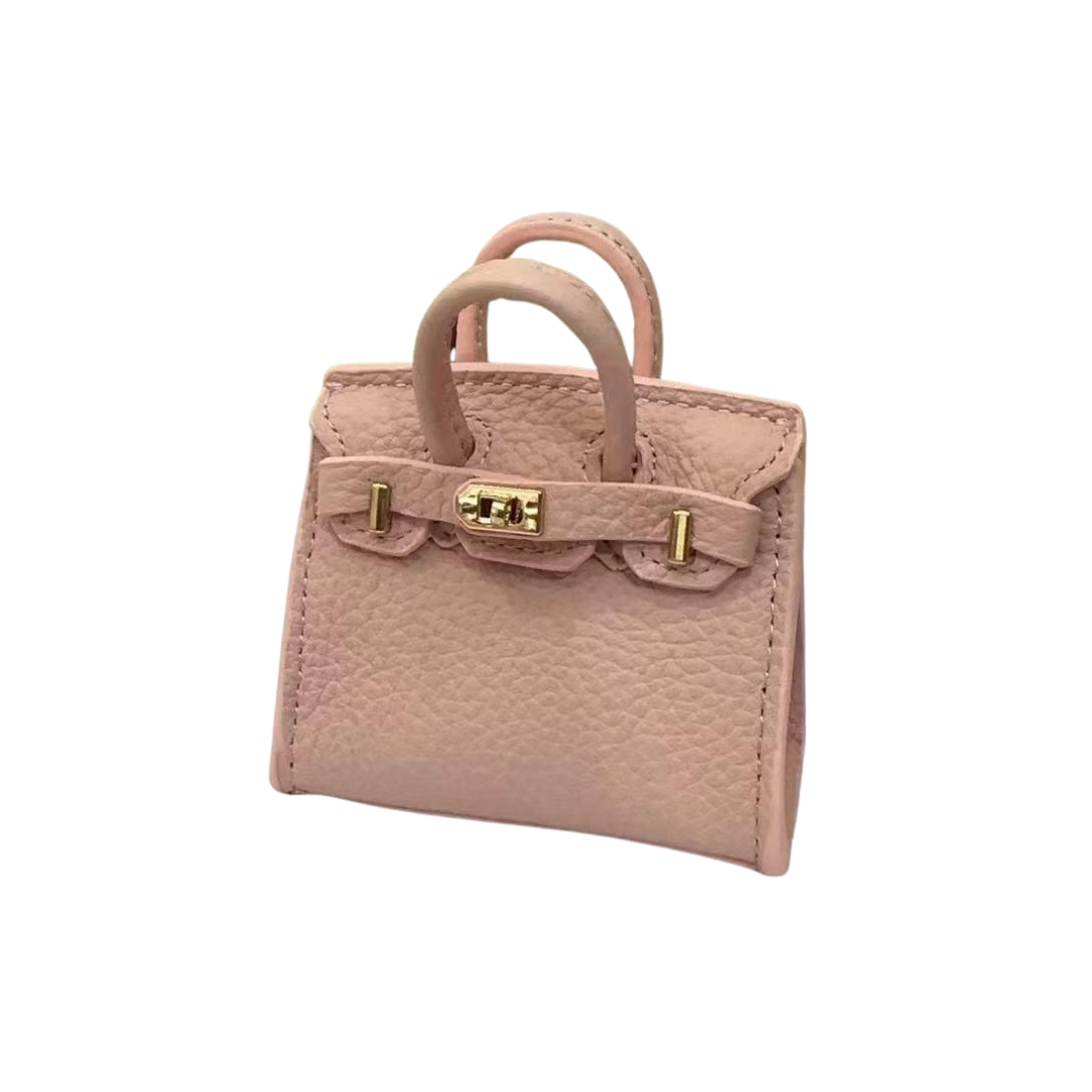Pink genuine leather structured bag charm with top handle, flap closure, securing straps, and gold-tone padlock hardware.