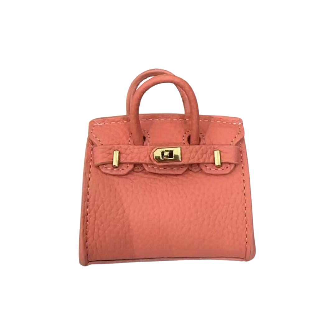 Rose (light pink/mauve) genuine leather structured bag charm with top handle, flap closure, securing straps, and gold-tone padlock hardware.