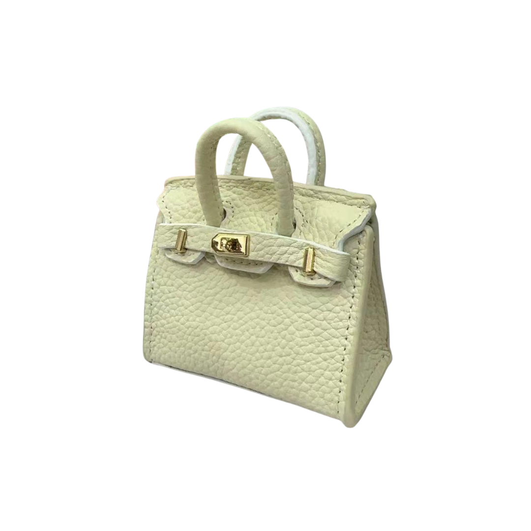 White genuine leather structured bag charm with top handle, flap closure, securing straps, and gold-tone padlock hardware.