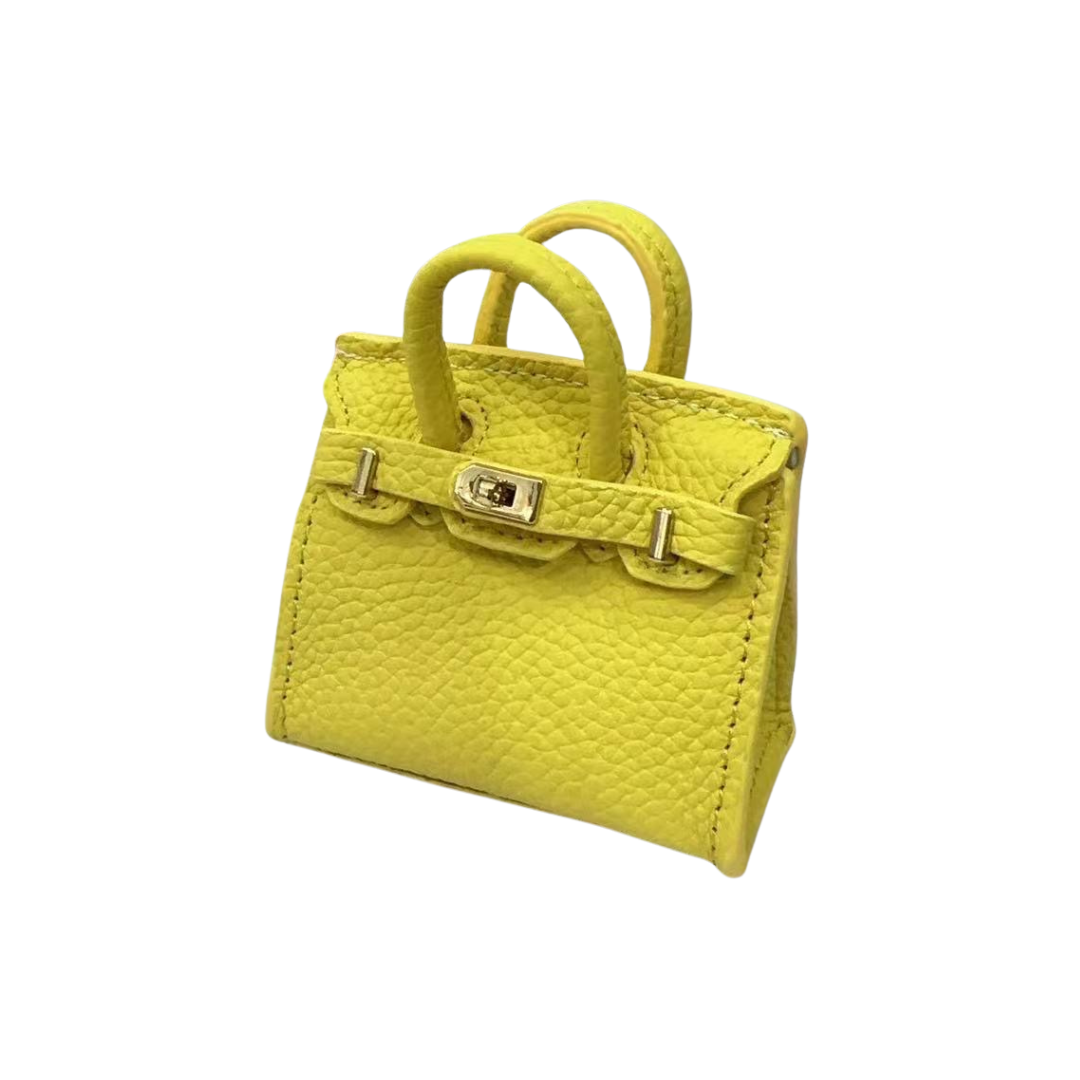 Yellow genuine leather structured bag charm with top handle, flap closure, securing straps, and gold-tone padlock hardware.