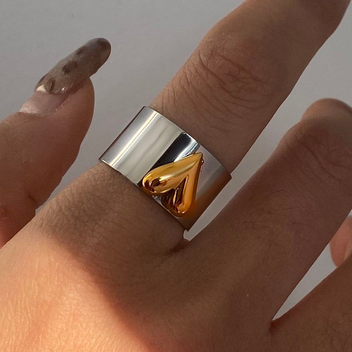 Gold and silver ring on a finger against a neutral background
