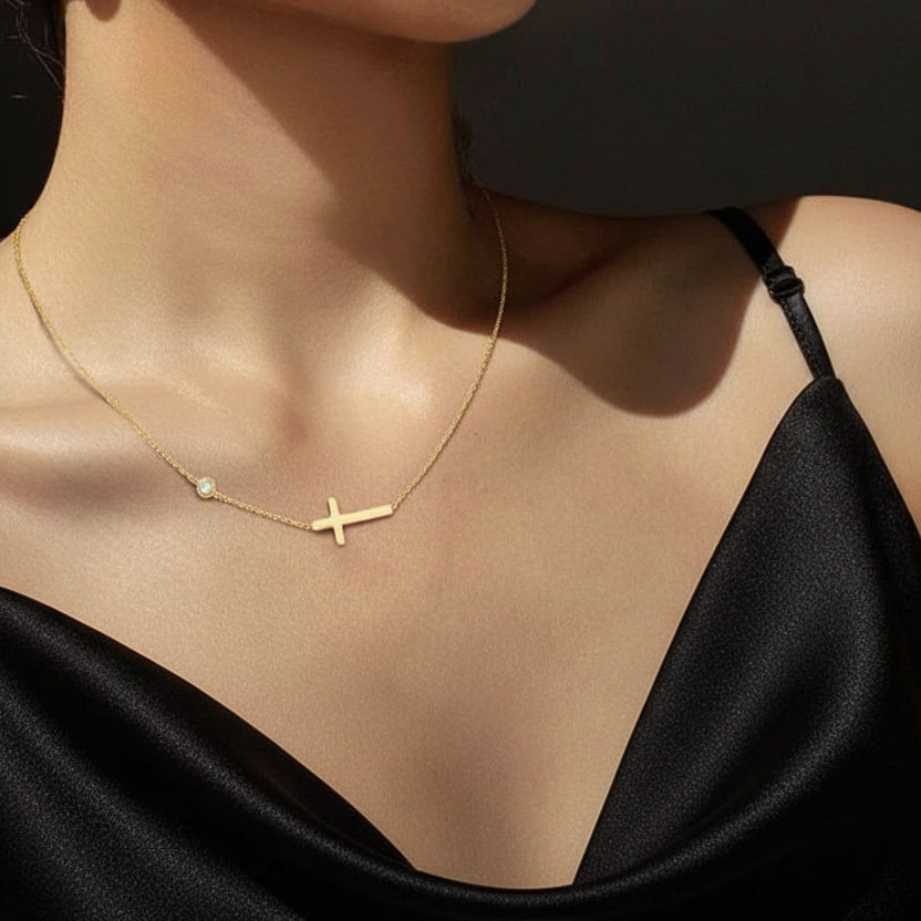Gold necklace with a cross pendant worn by a person in a white top.