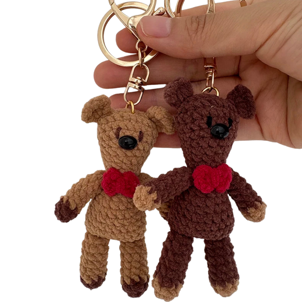 Two brown teddy bear keychains with red hearts held by a hand against a white background.