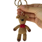Hand holding a small brown teddy bear keychain with a red bow tie against a white background