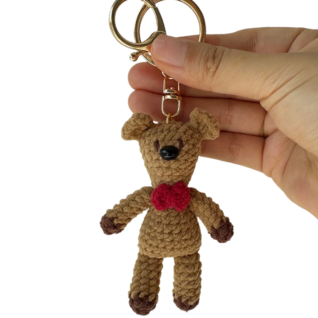 Hand holding a small brown teddy bear keychain with a red bow tie against a white background