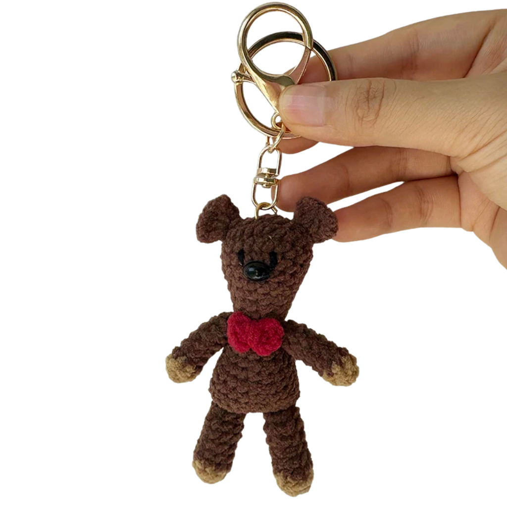 Hand holding a brown teddy bear keychain with a red heart on a white background