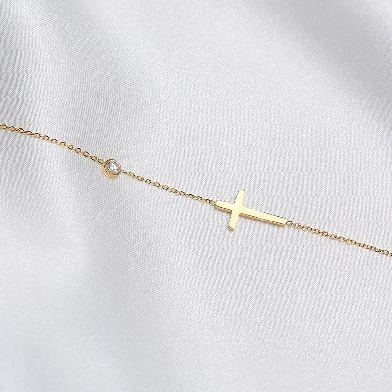 Gold bracelet with a small cross charm on a light gray background