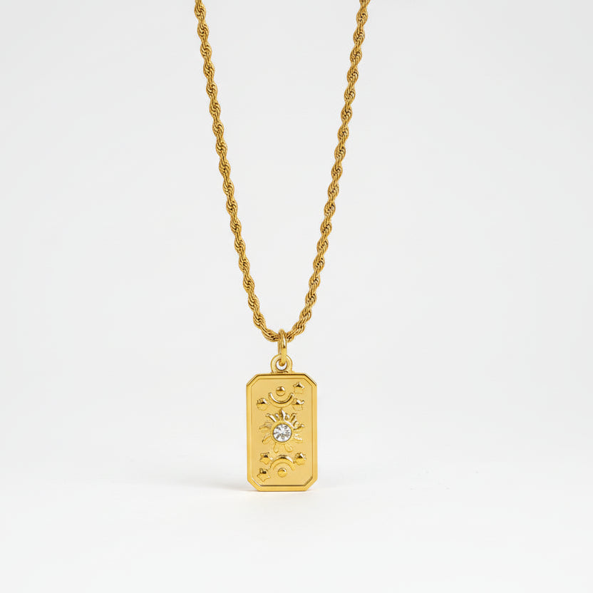 Gold necklace with a rectangular pendant on a textured stone surface
