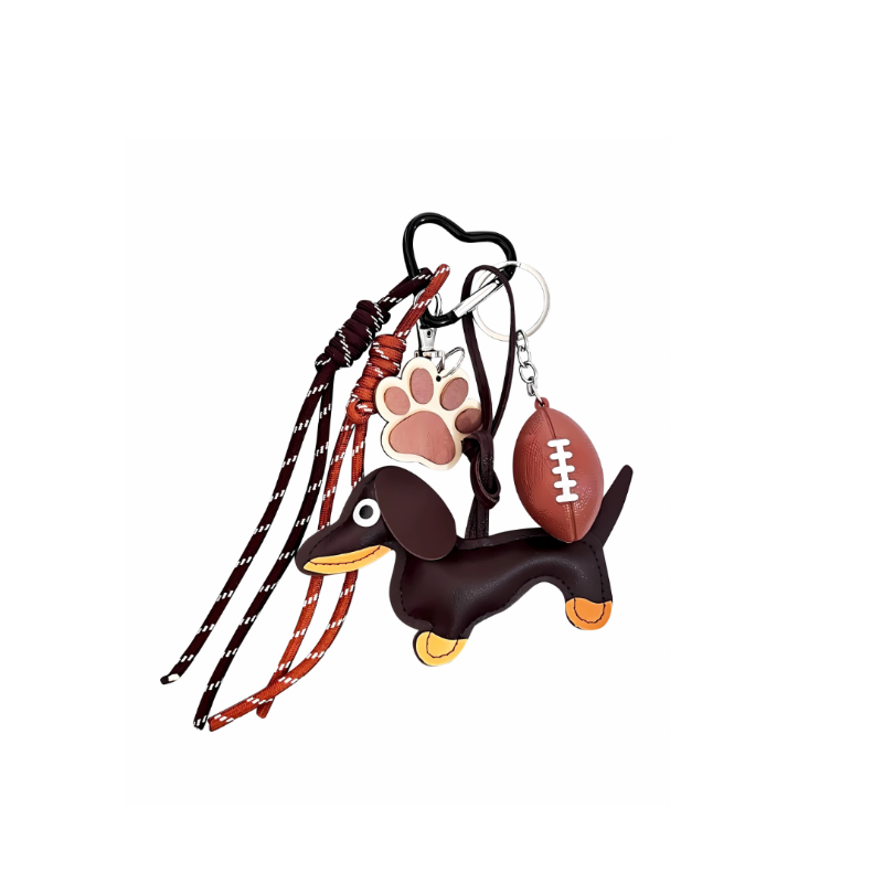 Brown leather Dachshund dog bag charm with a miniature football, leather paw print, and brown/orange cords hanging from a black heart-shaped keychain clip.