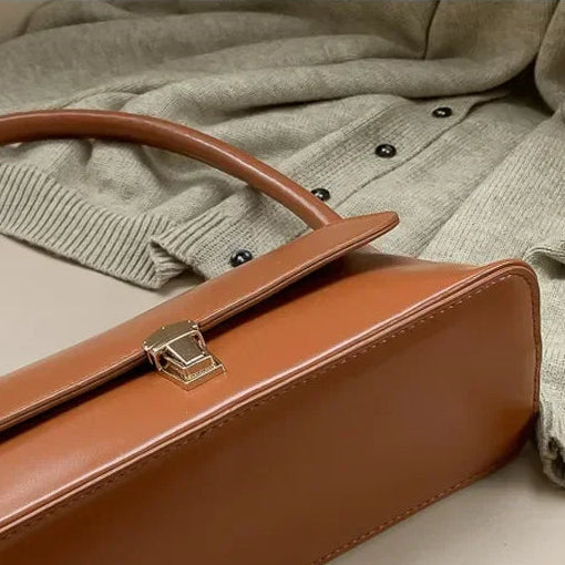 Brown handbag with a gold clasp on a textured surface