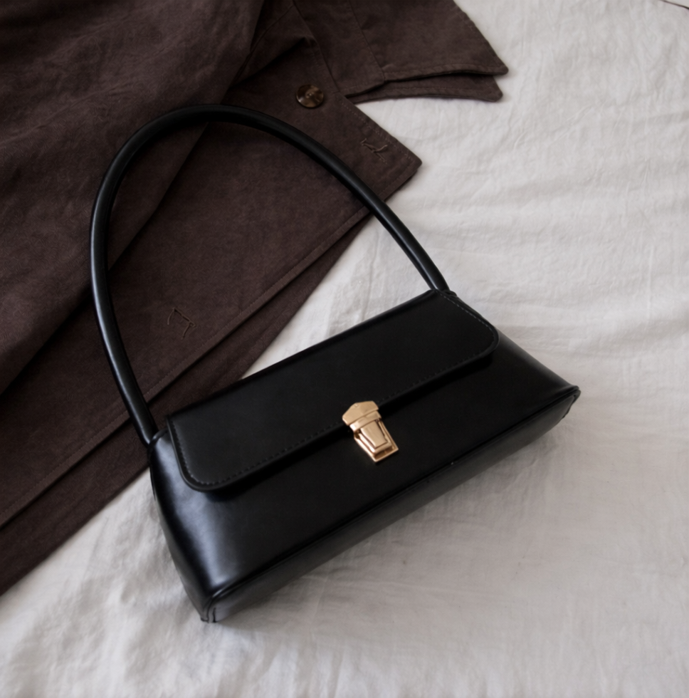 Black vegan leather handbag with a gold clasp on a white surface with a brown fabric background