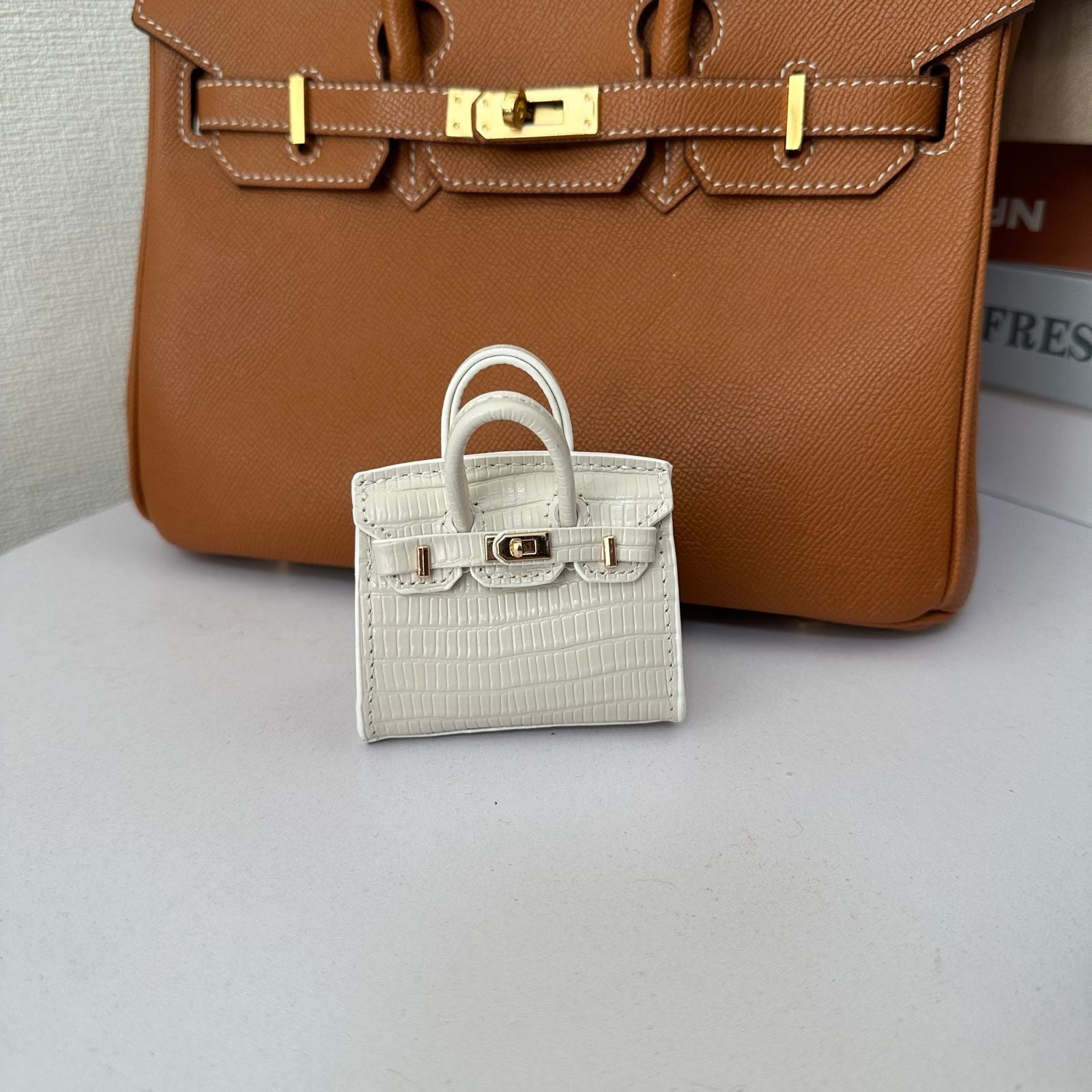 White genuine leather structured charm with a fine pebbled/grained texture and top handle.