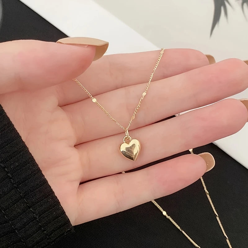 Gold heart-shaped pendant necklace on a hand against a neutral background