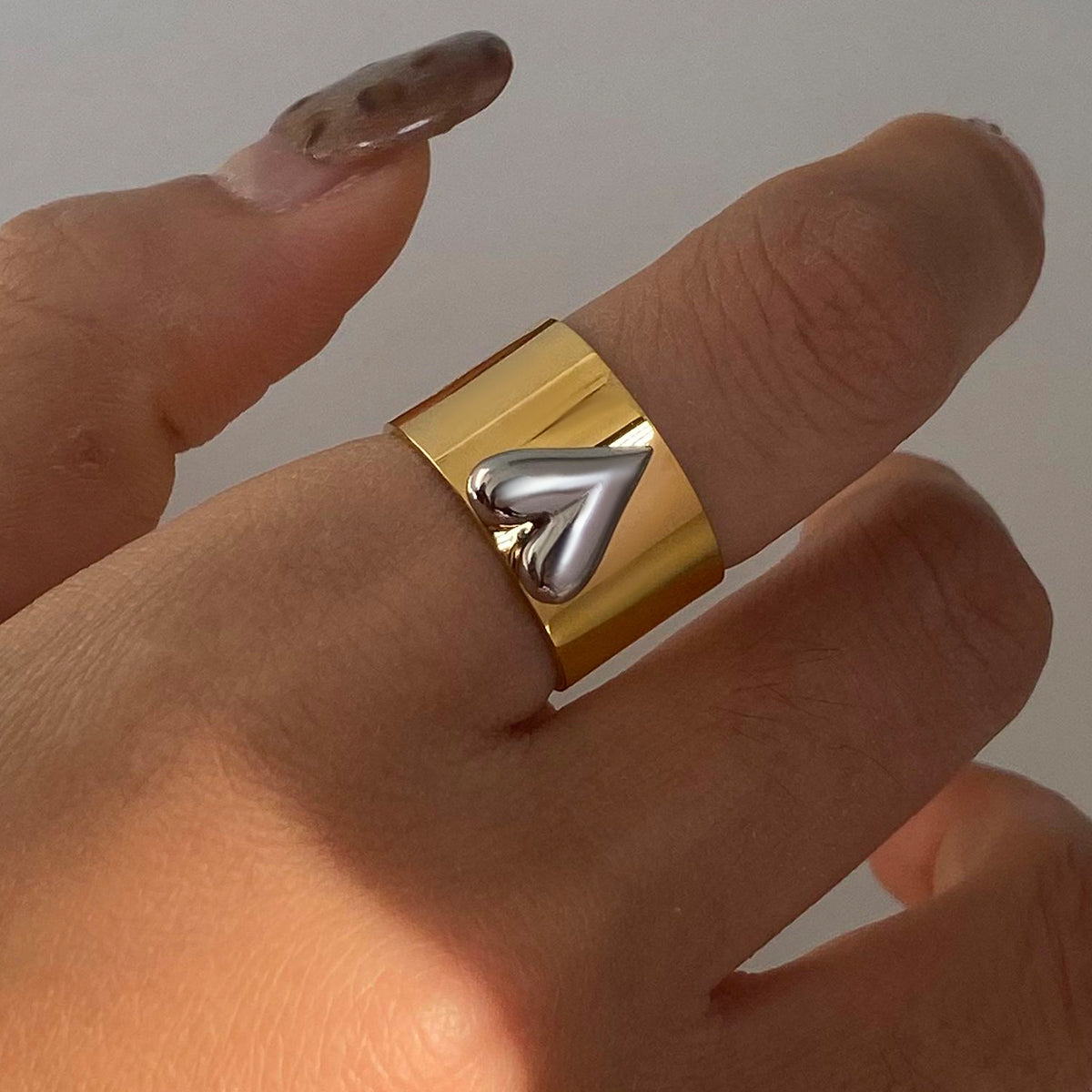 Gold ring with a silver design on a finger against a neutral background