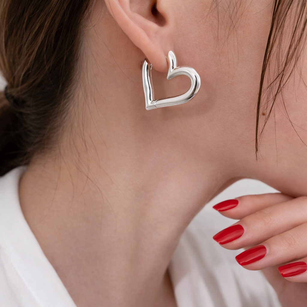 Silver heart-shaped hoop earring worn by a person with red nail polish.