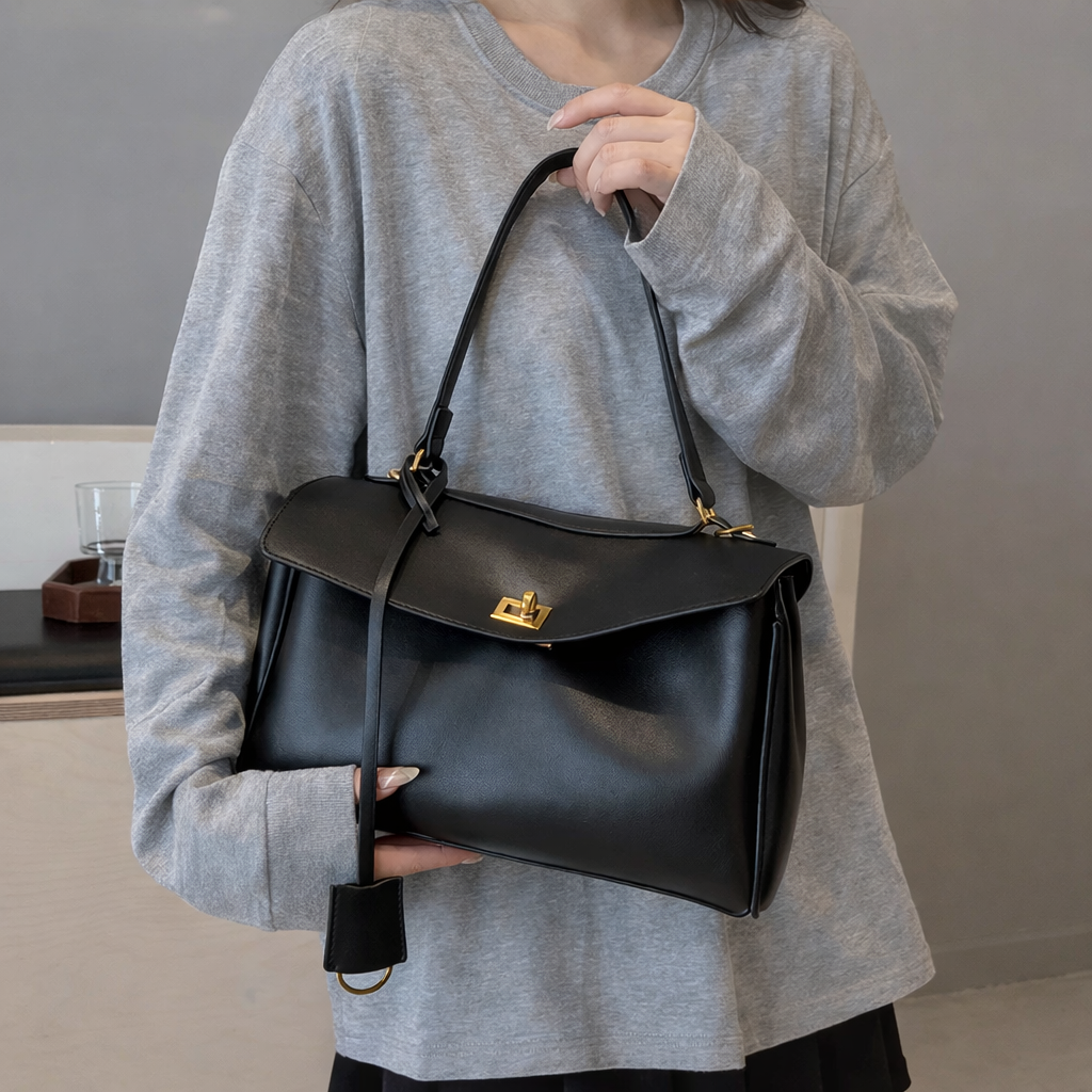 Person holding a black leather handbag against a neutral background
